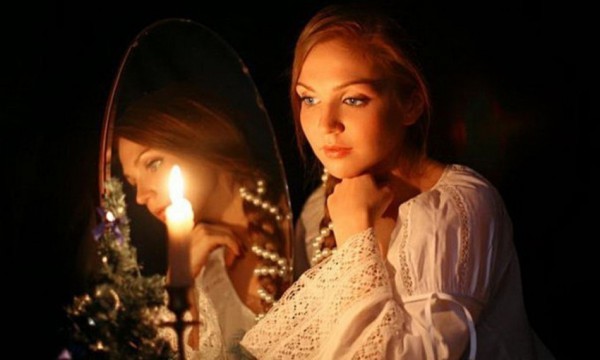 Девушка перед зеркалом со свечой в полной темноте